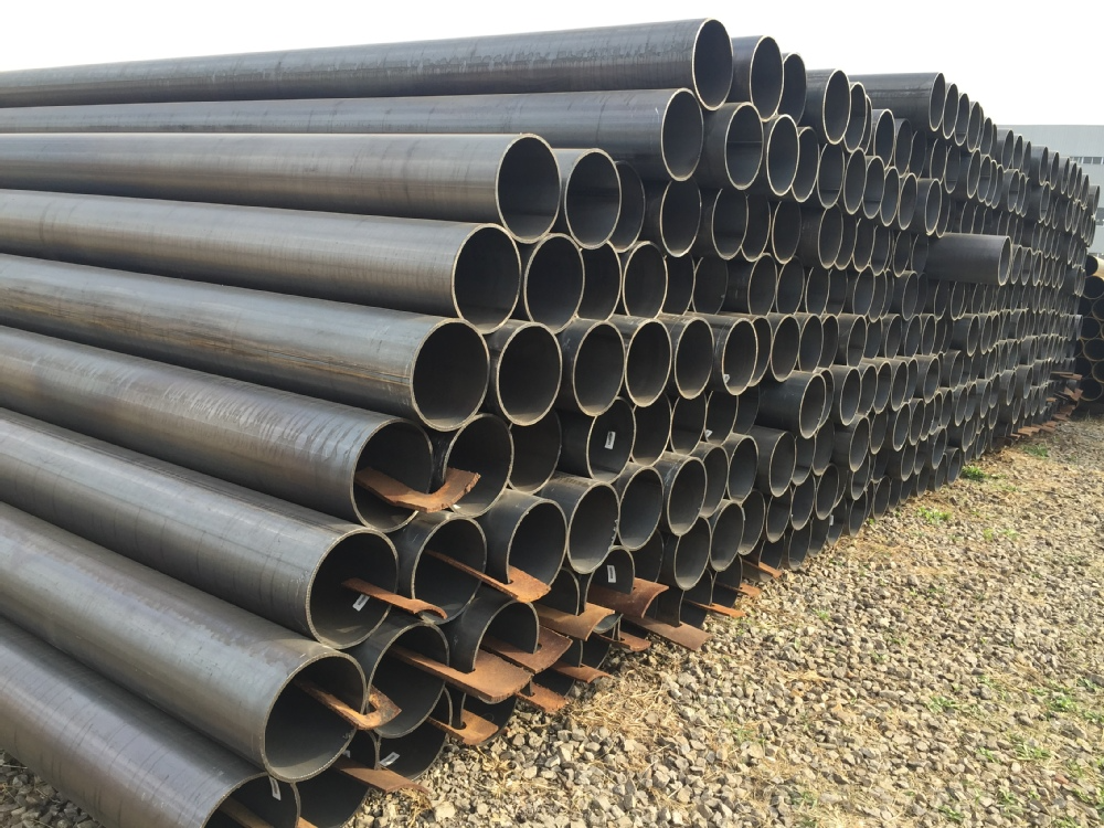 A substantial collection of mild steel pipes arranged in a field, surrounded by greenery and open space.